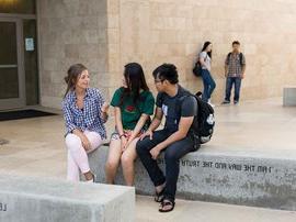 Students sitting and talking on stone bench.